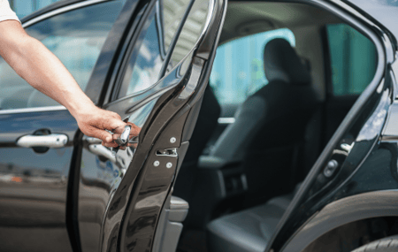 A taxi driver opens the back door of his black car for his client.