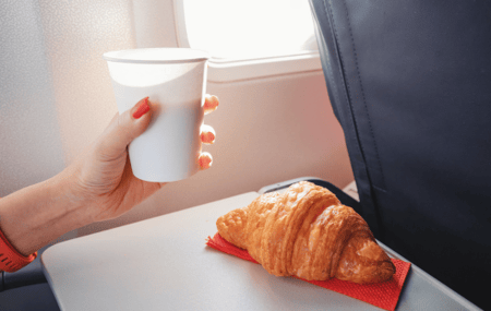 A woman enjoys a croissant and coffee aboard an airplane in the morning.