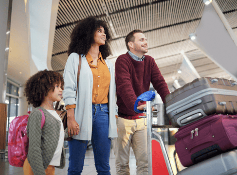 Deux parents marchent dans un aéroport en tenant la main de leur fille. 