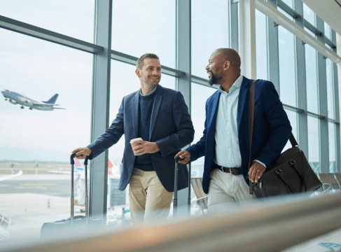 Two businesspeople walk through an airport with their suitcases in hand.