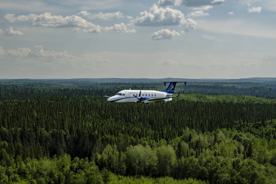 Un avion de Propair vol au dessus d'une forêt de conifères. 